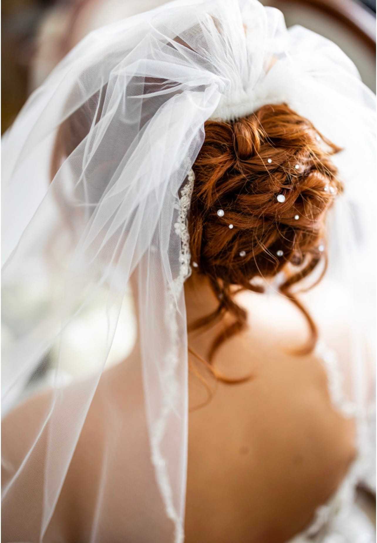 Bride with curled red hair adorned with pearls, wearing a white veil.