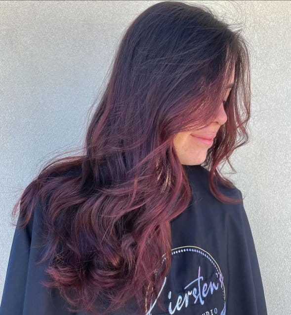 Wavy hair with deep burgundy highlights, styled by a salon professional.