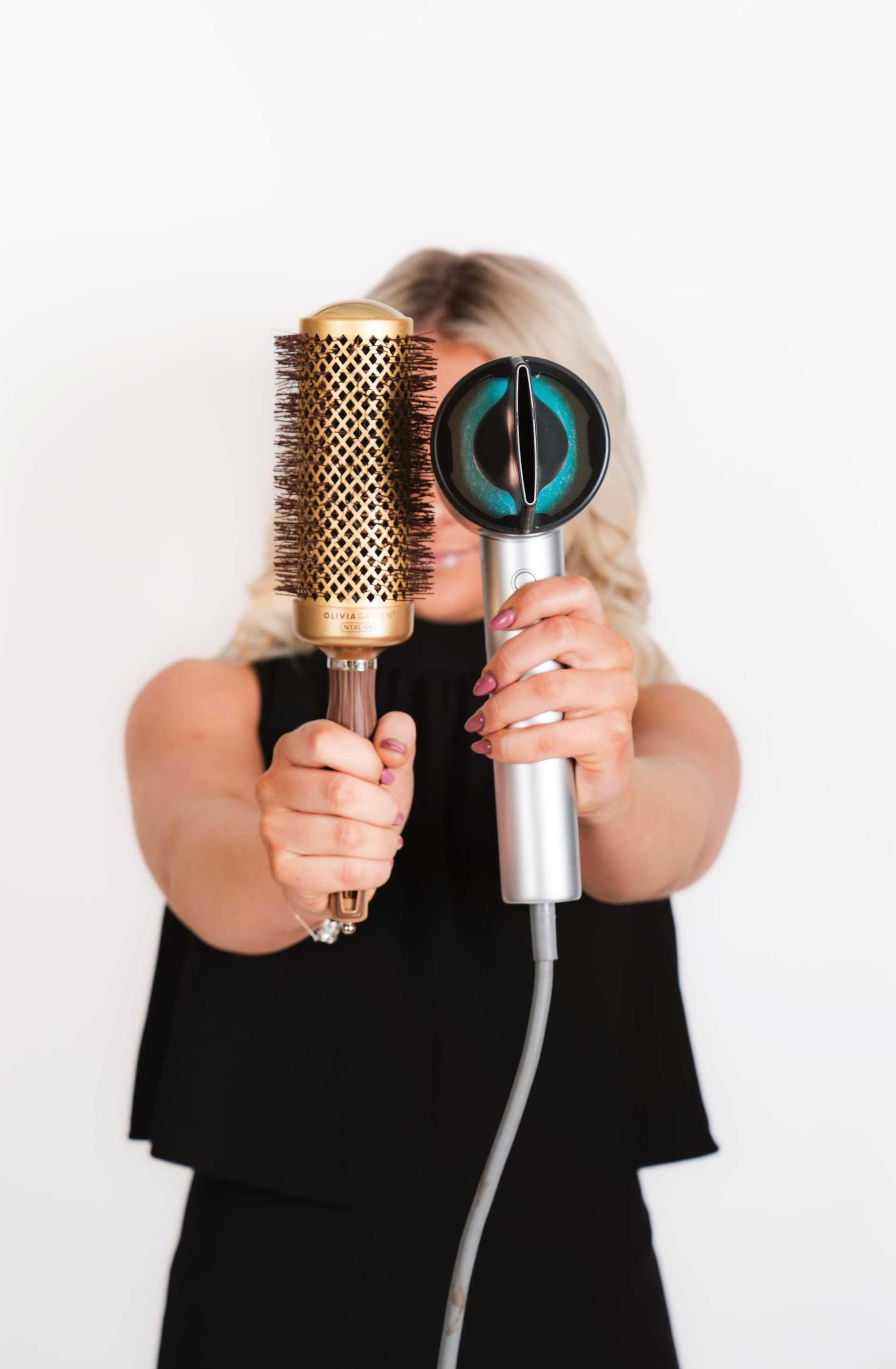 Person holding a round hairbrush and a hairdryer against a white background.